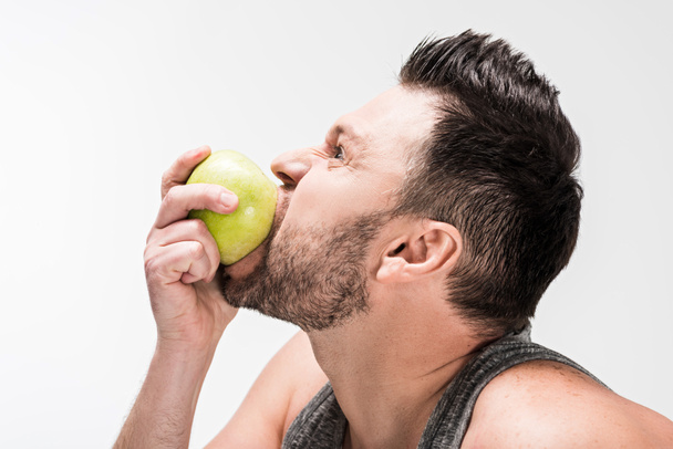 Widok z boku Chubby człowiek jeść zielone jabłko na białym tle - Zdjęcie, obraz