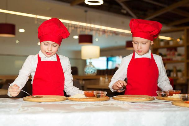 two beautiful cook girls in white shirts and red aprons in the restaurant make pizza - Фото, изображение