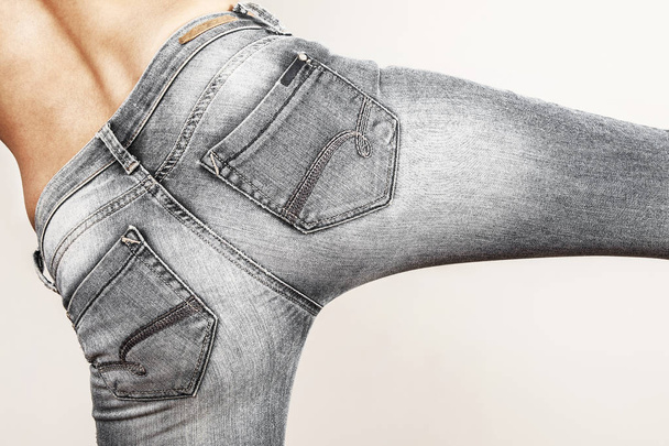 Beautiful woman is abdomen with jeans isolated on gray background - Zdjęcie, obraz