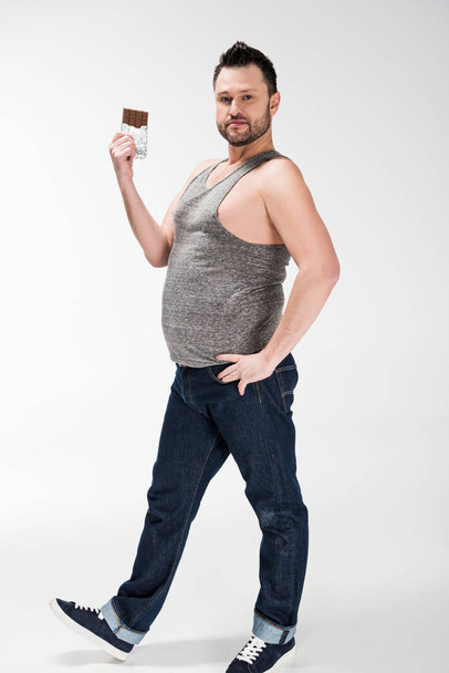 Übergewichtiger Mann blickt in Kamera und posiert mit Schokolade auf Weiß - Foto, Bild