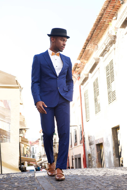 Full body portrait of african american male model in vintage suit and hat walking in city - Фото, изображение