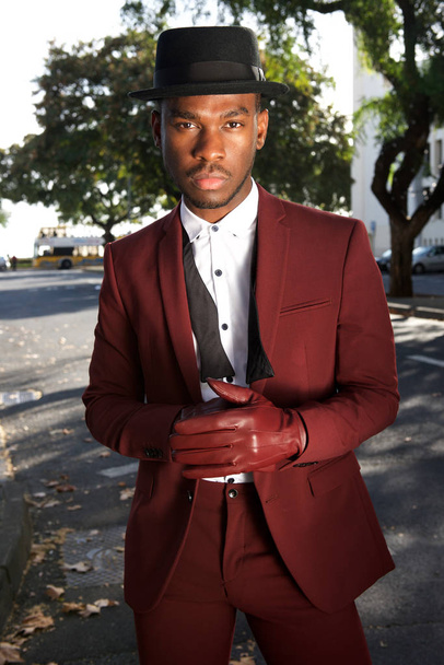Retrato de modelo de moda masculina afroamericana fresca posando en la calle de la ciudad con traje vintage y guantes
 - Foto, Imagen