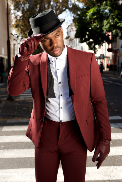 Retrato de modelo de moda masculina afroamericana fresca posando en la calle de la ciudad con traje vintage y sombrero
 - Foto, imagen