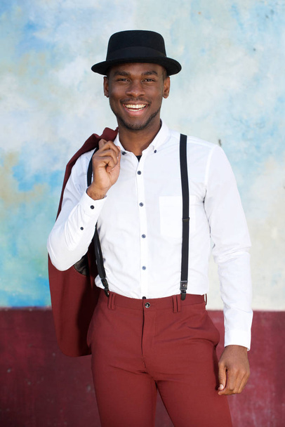 Portrait of handsome young black man in vintage suit and hat smiling by wall - Foto, Bild