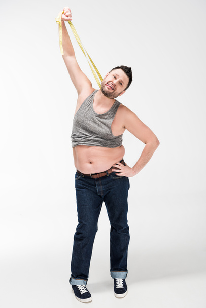 homem com sobrepeso colando a língua para fora e segurando fita métrica no branco
 - Foto, Imagem