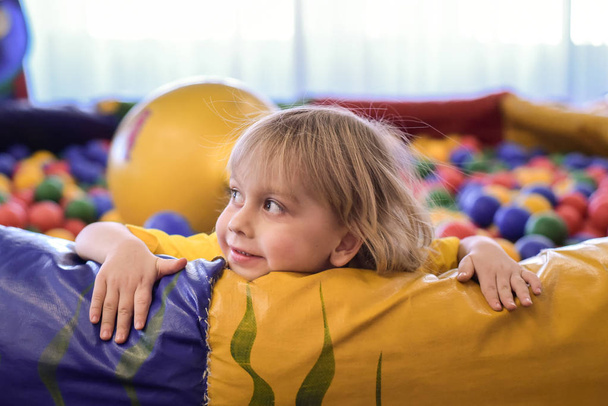 Retrato de un chico rubio con una camiseta amarilla. El niño sonríe y juega en la sala de juegos de los niños. Piscina de pelota
. - Foto, imagen
