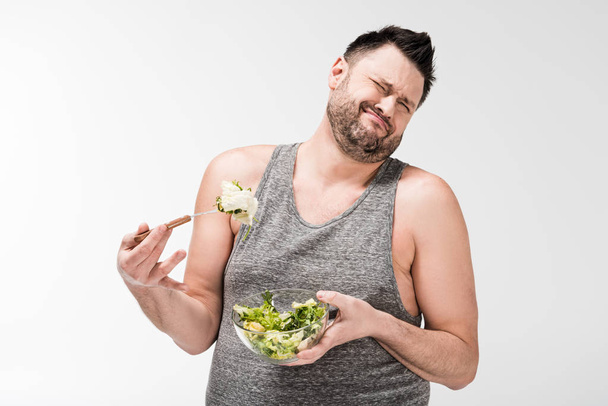 サラダのボウルを持ち、顔の表情を白に隔離する不愉快な太りすぎの男 - 写真・画像