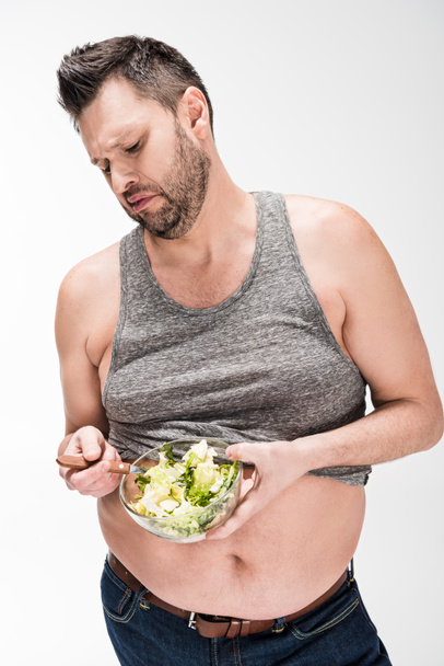 Unzufriedener übergewichtiger Mann hält Schüssel mit Salat auf weiß - Foto, Bild