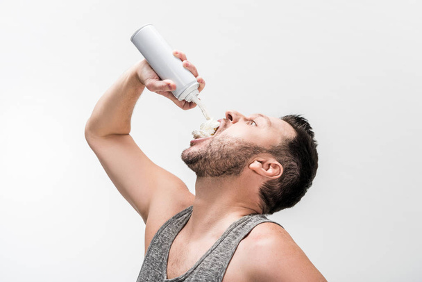 chubby man in tank top spraying whipped cream in mouth on white - 写真・画像