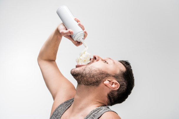 chubby man spraying whipped cream in mouth on white - Foto, afbeelding