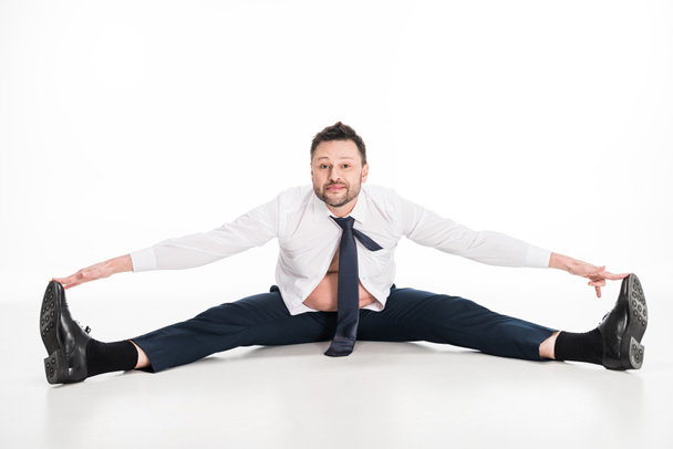 overweight man in tight formal wear sitting with outstretched legs and looking at camera on white - Foto, afbeelding
