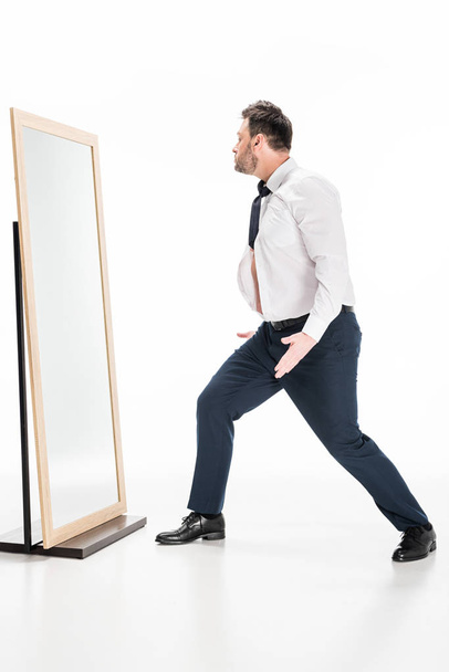 Nadváha muže při formálním nošení gestikulování při pohledu na zrcadlo na bílém - Fotografie, Obrázek