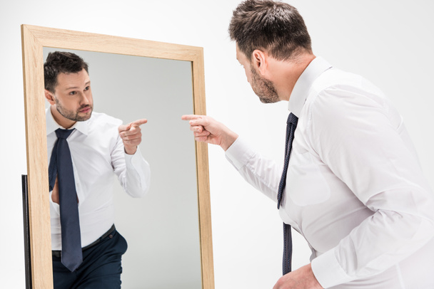 człowiek z nadwagą w formalne zużycie wskazując palcem na odbicie w lustro na białym - Zdjęcie, obraz
