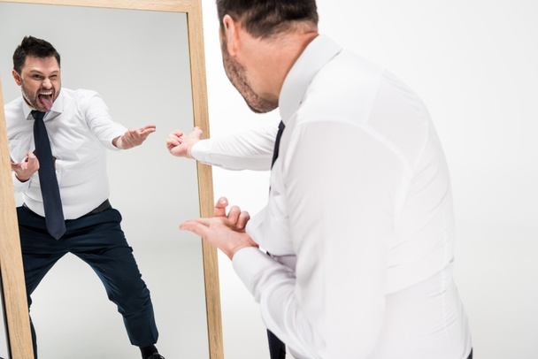 muž s tlustouši při formálním nošení strkal jazyk při pohledu na zrcadlo izolované na bílém - Fotografie, Obrázek