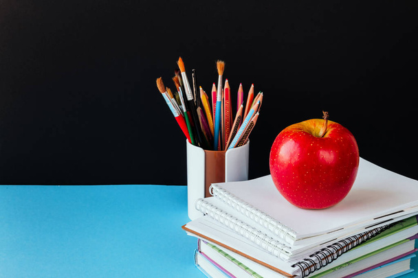 School accessories, notepad, pencils, markers, apple. Concept back to school on a blue background with copy space for text - Φωτογραφία, εικόνα