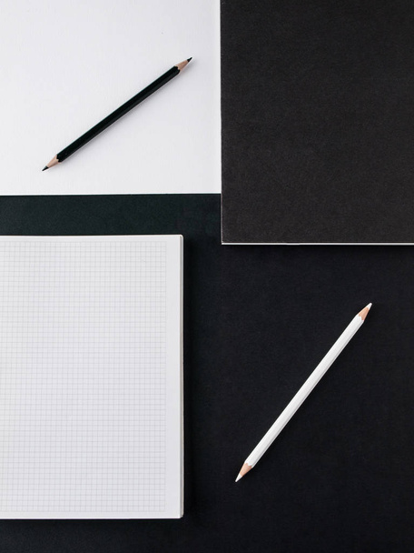 Concepto de oficina. Lápices en blanco y negro, cuaderno en blanco y revista en negro sobre un fondo de papel blanco y negro. Vista superior. Copiar espacio
 - Foto, Imagen