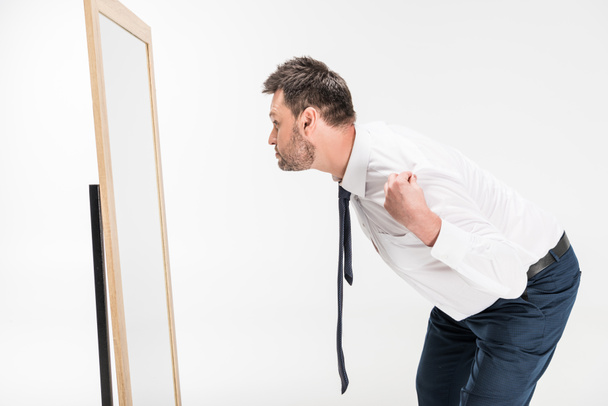 overweight man in formal wear bending over and looking at mirror isolated on white - Fotografie, Obrázek