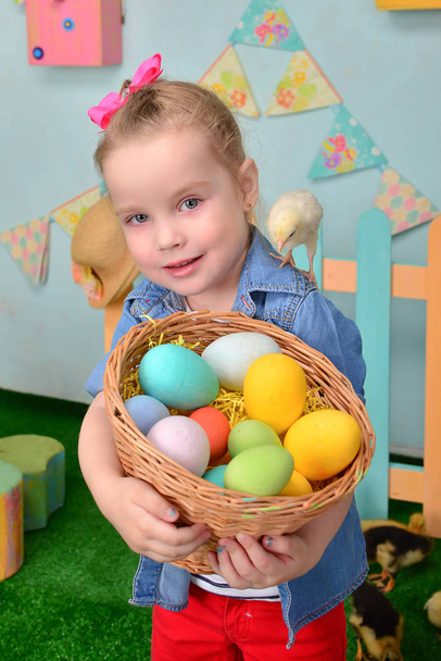 Мила усміхнена дівчинка з кошиком, повним різнокольорових великодніх яєць. Пташеня на плечі
 - Фото, зображення