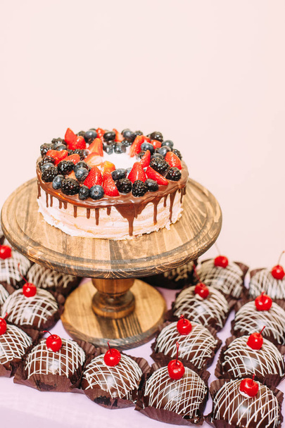 Bright chocolate wedding cake decorated with fresh fruits and berries on wooden surface. A lot of chocolate cakes with cherries. Dessert made from natural ingredients - Φωτογραφία, εικόνα