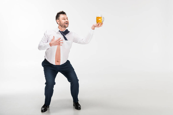 mosolygó túlsúlyos ember feszes inget gazdaság pohár sört és geszturing kézzel fehér és másolási tér - Fotó, kép