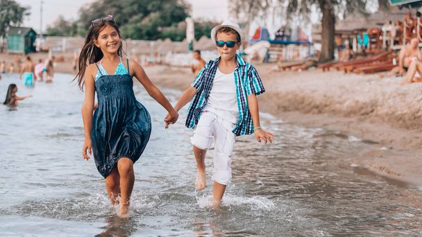 Pieni poika ja tyttö kävelevät yhdessä pitkin rantaa ja pitävät
 - Valokuva, kuva