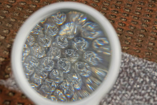 Μεγεθυντικός φακός αυξάνει τη συσκευασία του σελοφάν στα σπυράκια σε ένα καφέ τραπέζι - Φωτογραφία, εικόνα