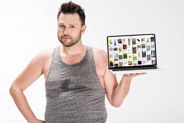 overweight man looking at camera and holding laptop with pinterest website on screen isolated on white - Foto, Imagem