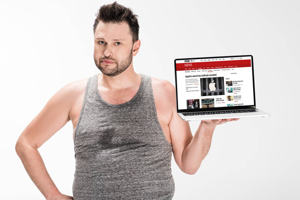 overweight man looking at camera and holding laptop with bbc news website on screen isolated on white - 写真・画像