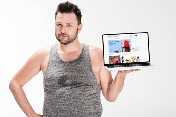 overweight man looking at camera and holding laptop with ebay website on screen isolated on white - 写真・画像