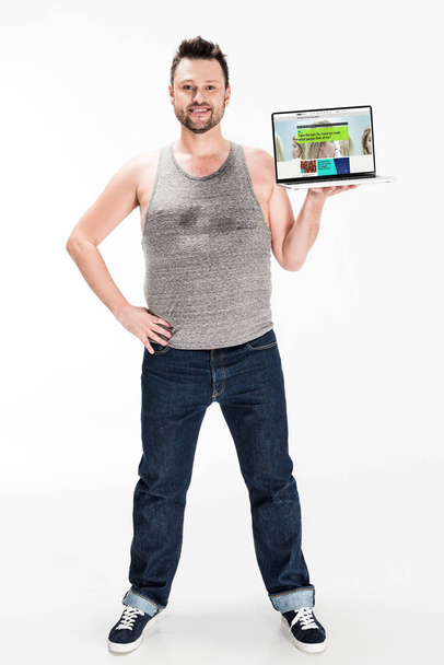 smiling overweight man looking at camera and presenting laptop with bbc website on screen isolated on white - Foto, immagini
