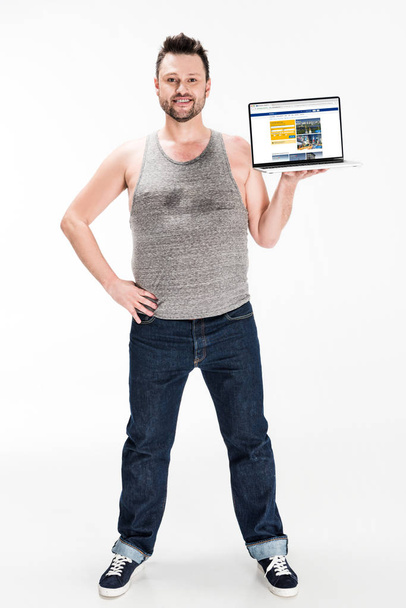 lachend overgewicht man kijken naar camera en presenteren laptop met boeking website op het scherm geïsoleerd op wit - Foto, afbeelding