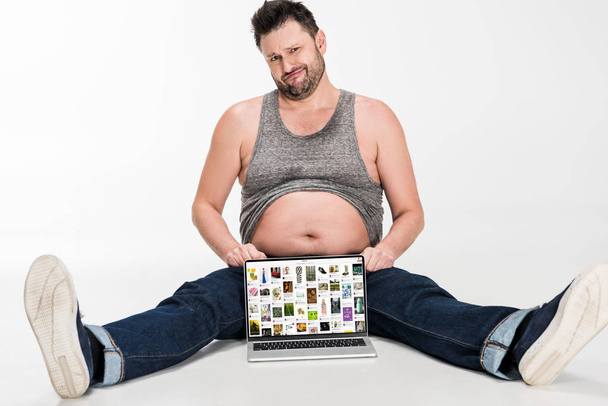 sceptyczny człowiek z nadwagą co wyraz twarzy i siedzi z laptopem z witryną Pinterest na ekranie białym na białym tle - Zdjęcie, obraz