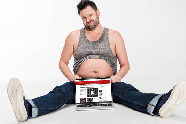 skeptical overweight man making facial expression and sitting with laptop with bbc news website on screen isolated on white - Photo, Image