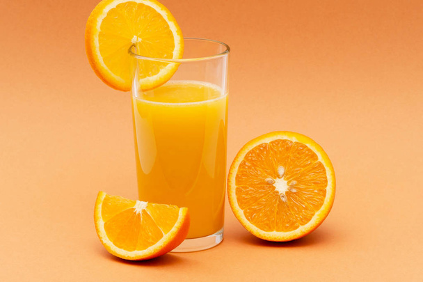 een glas jus d'orange op een oranje achtergrond met een plakje oranje - Foto, afbeelding