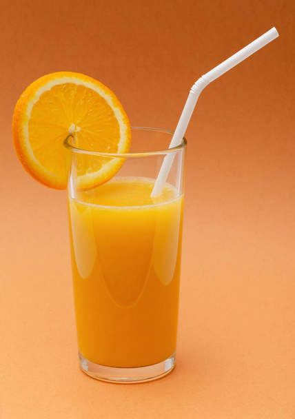 ein Glas Orangensaft auf orangefarbenem Hintergrund mit einem Strohhalm und einer Scheibe Orange - Foto, Bild