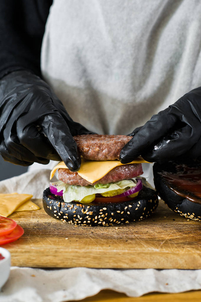 As mãos do chef cozinham o hambúrguer. O conceito de cozinhar cheeseburger preto. Receita de hambúrguer caseiro. Cozinha, vista lateral, espaço para texto
 - Foto, Imagem