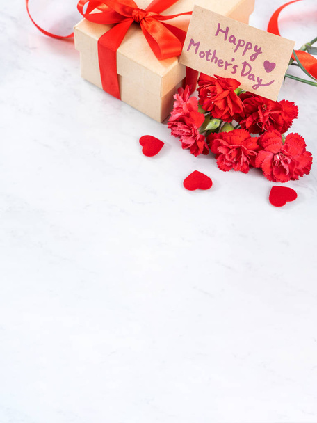 May mothers day handmade giftbox wishes photography - Beautiful blooming carnations with red ribbon bow box isolated on modern marble desk, close up, copy space, mock up - Photo, image