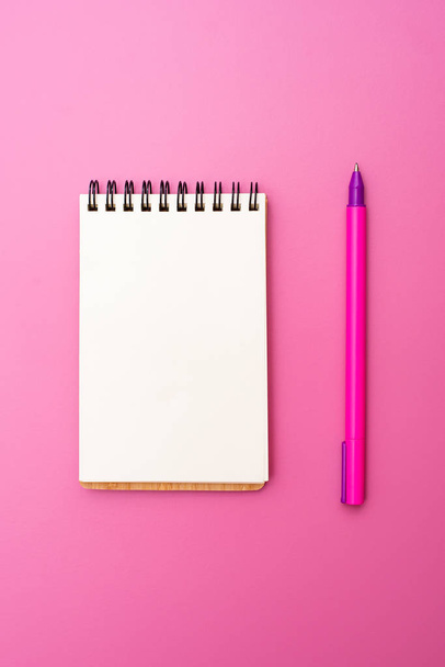 Caderno em branco com espiral para a aplicação de etiquetas e caneta sobre fundo rosa
 - Foto, Imagem