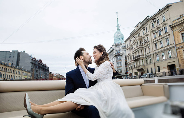 stylish bride and groom on their wedding day, having fun and kissing on a boat trip on the river  - 写真・画像