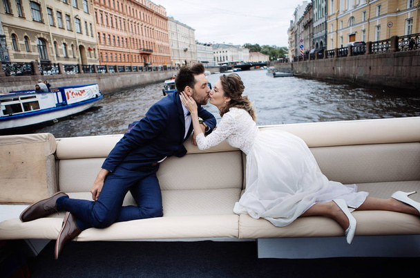 stylish bride and groom on their wedding day, having fun and kissing on a boat trip on the river  - Фото, изображение