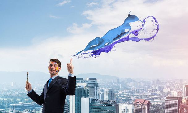 Successful businessman in black suit gesturing and smiling while standing with blue coloured splash against cityscape view on background. - Photo, Image