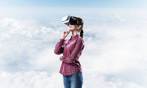 Young caucasian woman in virtual reality helmet against day sky background - 写真・画像