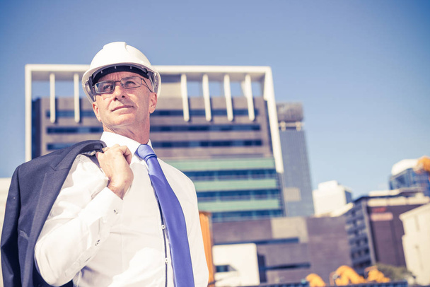 Confident construction engineer in hardhat and with jacket on shoulder - Zdjęcie, obraz
