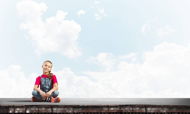 Aranyos gyerek lány ül, épület tető, és keresi a kamera - Fotó, kép