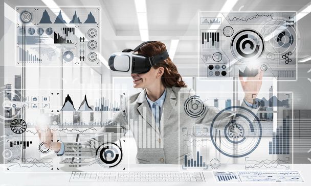 Horizontal shot of young successful business woman sitting inside office and using virtual reality headset with digital media interface - Foto, Bild