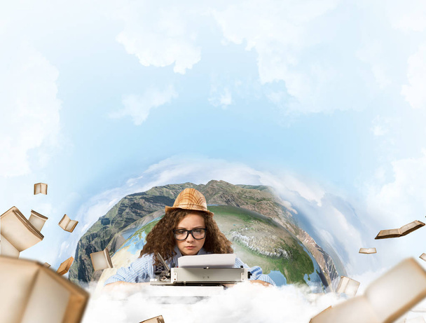 Portrait of hard-working female writer using typing machine while sitting at the table with flying papers and Earth globe among cloudy skyscape on background. Elements of this image furnished by NASA - Photo, Image