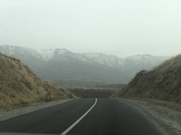 Camino de montaña. Viaje por carretera. Las cimas de las montañas rocosas están cubiertas de nieve. Un viaje a la naturaleza en invierno
. - Foto, Imagen