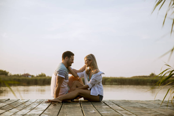 Kochająca para siedzi na molo na jeziorze w lecie zachodu słońca - Zdjęcie, obraz