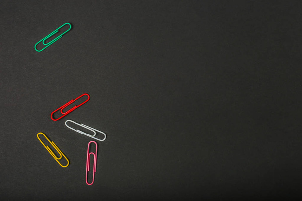 Color paper clips on black background. Top view. Flat lay. Free space - Фото, изображение