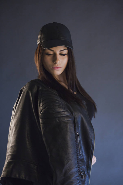 studio shot of stylish brunette woman wearing leather cap and posing on camera, looking down  - Фото, зображення
